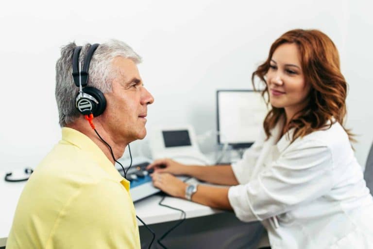 audiology patient completing hearing test Man in an audiologists office with headphones on listening intently during a hearing test